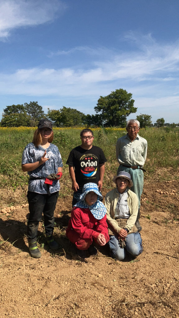 畑に5名が笑顔で立っており、手前の2名はしゃがんでいる